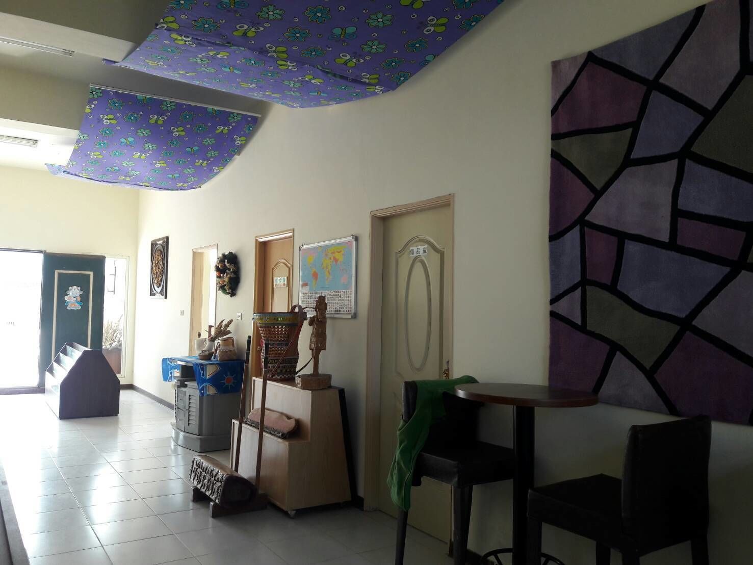A room with a tiled floor, a desk, a chair, a small table, and a wall with a geometric pattern.