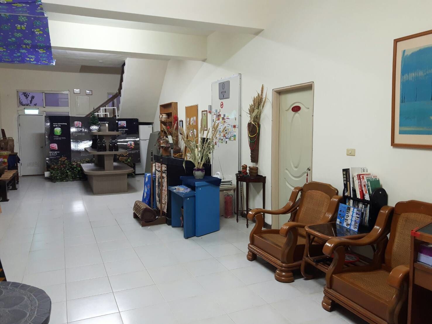 A spacious living area with a staircase leading to an upper floor, a coffee table, several chairs, a bookshelf, and a framed picture on the wall.
