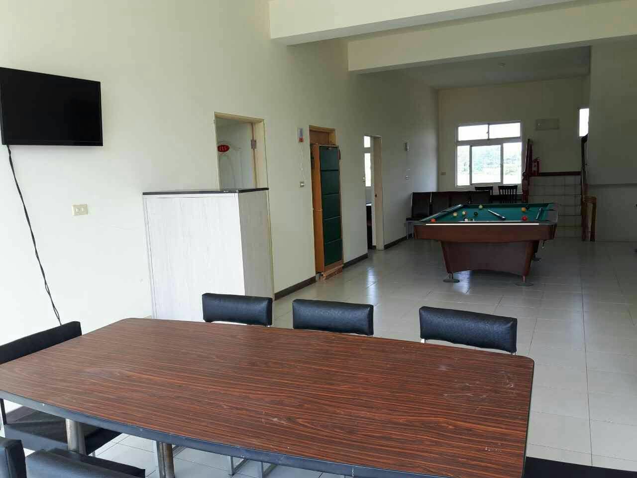 Una habitació amb billar, taula de menjador i cadires, i televisió penjada a la paret.