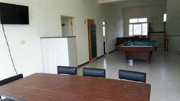 Una habitació amb billar, taula de menjador i cadires, i televisió penjada a la paret.