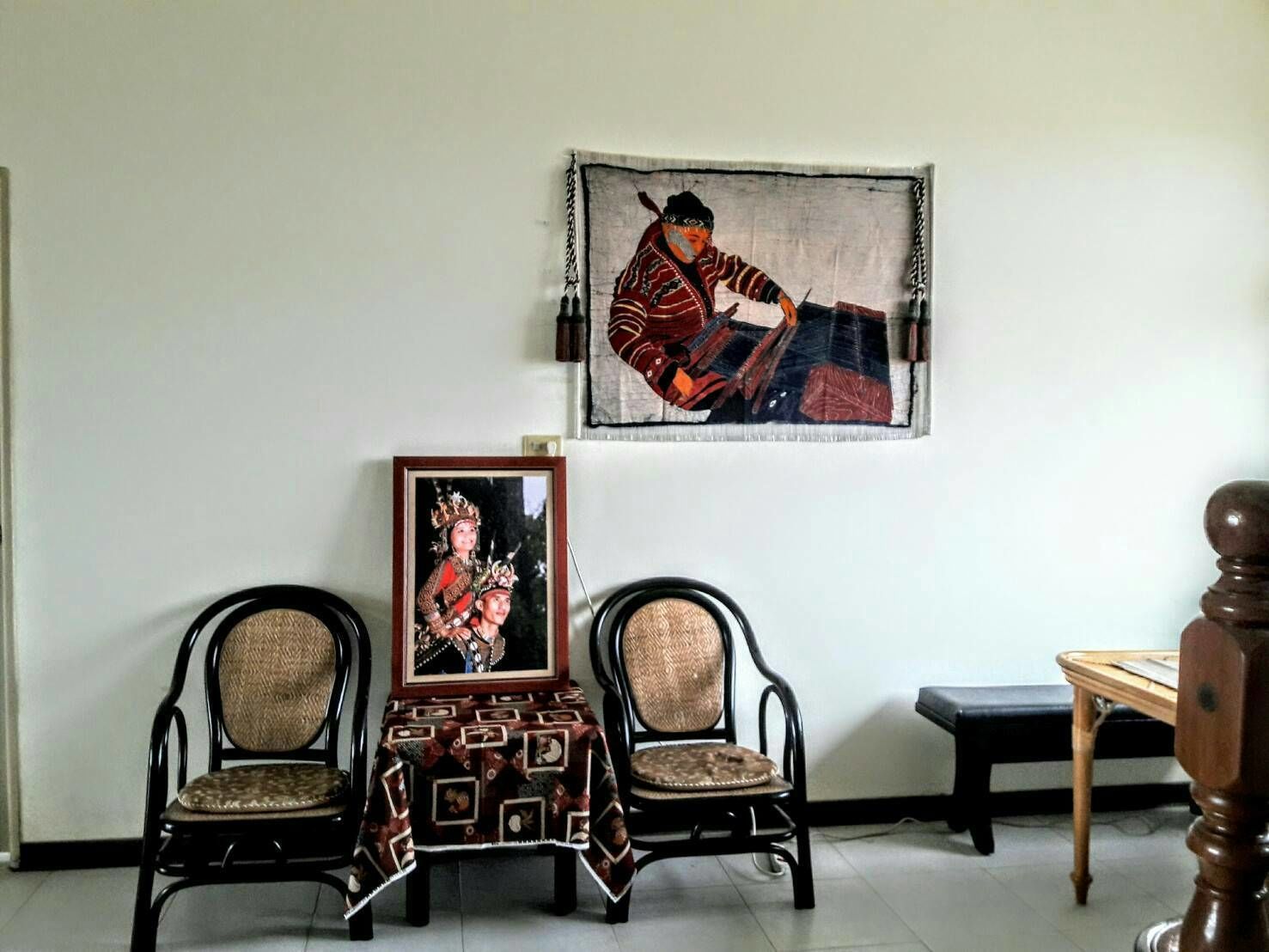 Une pièce comprenant deux fauteuils en osier, une petite table et un tableau encadré accroché au mur.