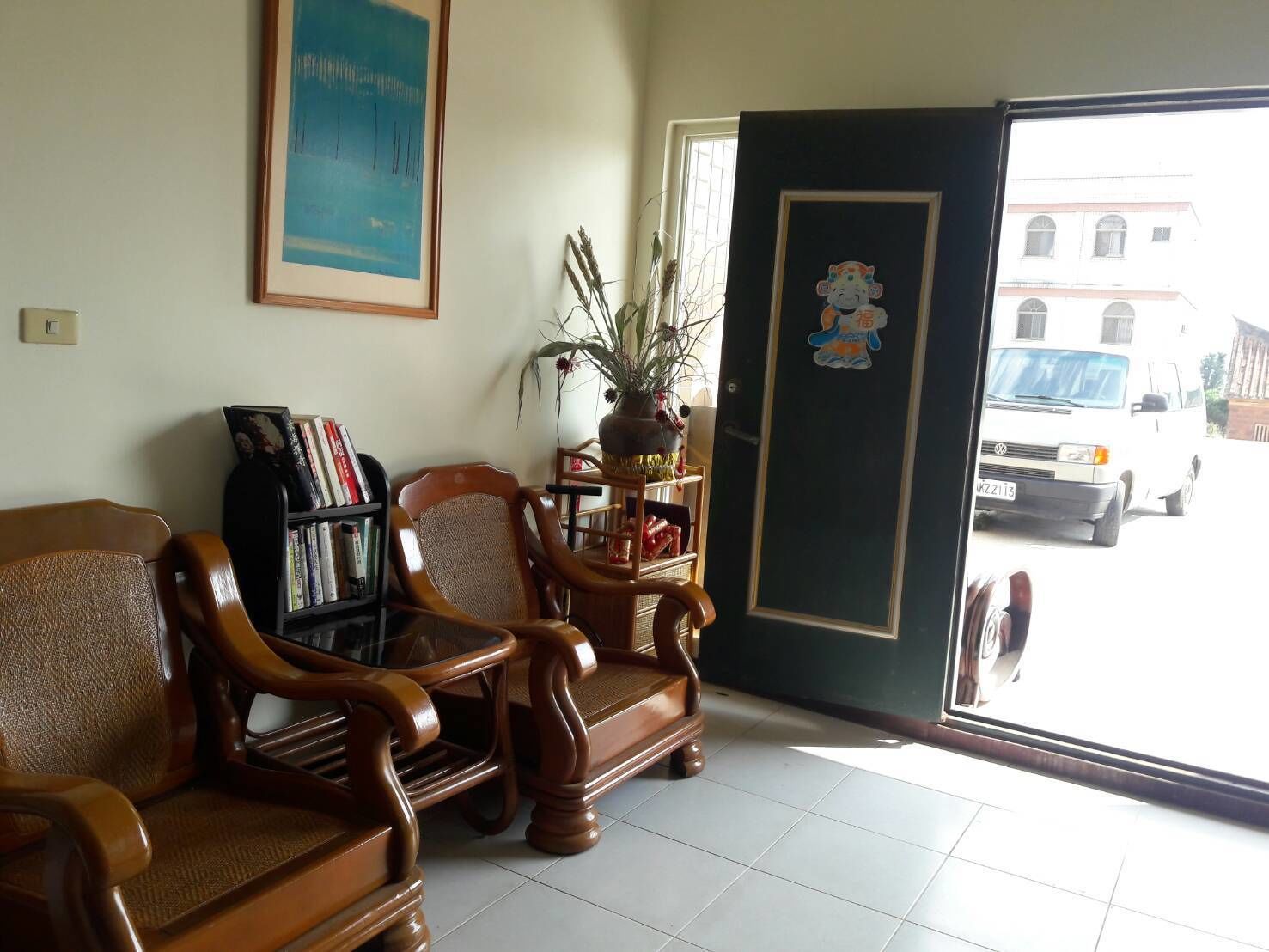 A reception area with wooden chairs, a bookshelf, a potted plant, and a door with a sticker.