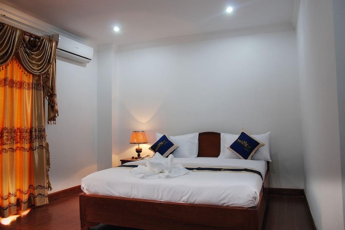 Une chambre d’hôtel avec un lit, des oreillers, une lampe de chevet et un rideau.