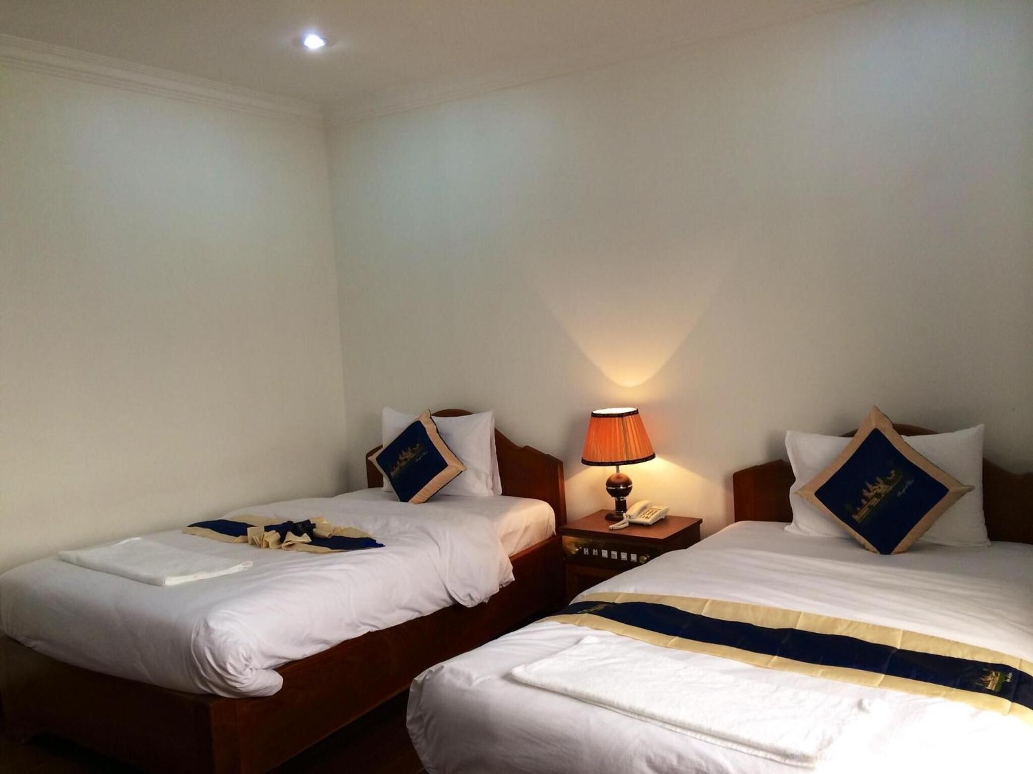 Een hotelkamer met twee éénpersoonsbedden, elk met een blauw en wit kussen, een bedlampje en een klein tafeltje met een telefoon.