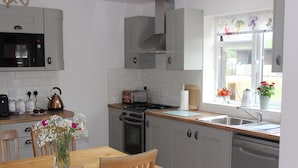 Una cocina con microondas, estufa, horno y lavavajillas. Hay una mesa de comedor con sillas y un florero con flores.