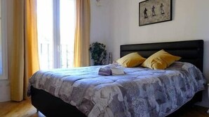 Ein Schlafzimmer mit einem Bett, Holzboden, einem Fenster mit Vorhängen und einem gerahmten Bild an der Wand.