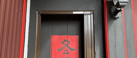 Una puerta tradicional con un letrero rojo, un aldabón de metal y un farol a la derecha.