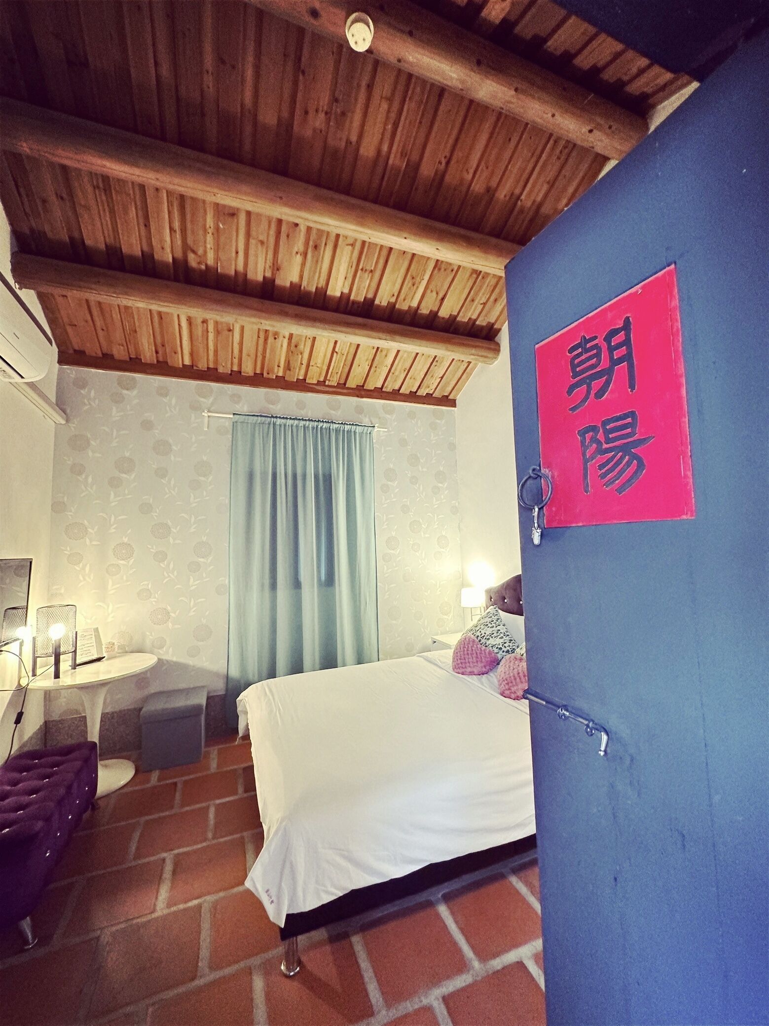 A bedroom with a wooden ceiling, a bed with white bedding, a blue wall, and a red sign with Chinese characters.
