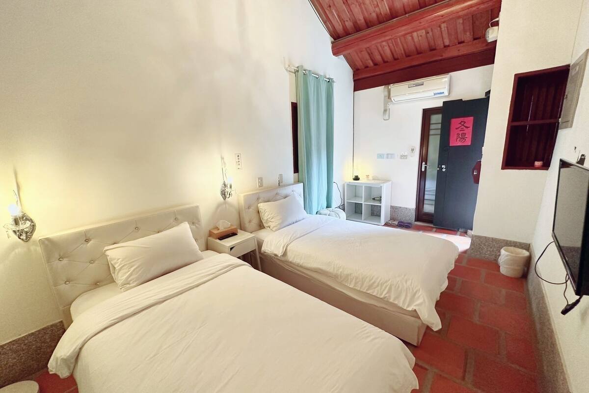 A hotel room with two beds, a small table, a TV, and a bathroom.