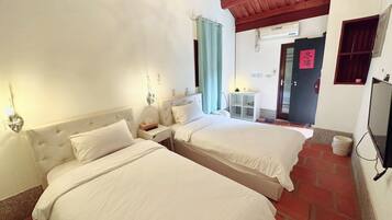 Habitación de hotel con dos camas, una mesita pequeña, televisor y baño.