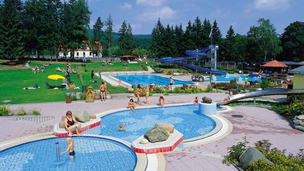 A swimming pool area with multiple pools, a water slide, and a grassy area with people. - Modern comfort apartment in the spa town on the Rennsteig (Friedrichroda OT Finsterbergen)
