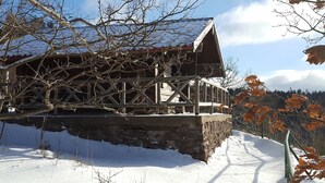 A wooden cabin with a stone foundation, surrounded by snow and autumn foliage. - Modern comfort apartment in the spa town on the Rennsteig (Friedrichroda OT Finsterbergen)