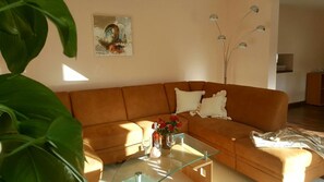 Un salon avec un canapé marron, une table basse en verre et un tableau accroché au mur.
