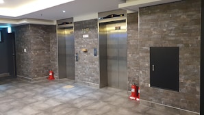 A modern elevator area with two elevators, a fire extinguisher, and a tiled floor. - CNN Hotel (Changwon)