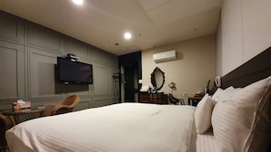 A hotel room with a large bed, a flat-screen TV mounted on the wall, a dresser, a mirror, and a small table with a chair. - CNN Hotel (Changwon)