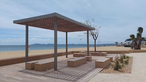 En paviljong vid stranden med ett tak täckt av tegelpannor, sittplatser och utsikt över havet.