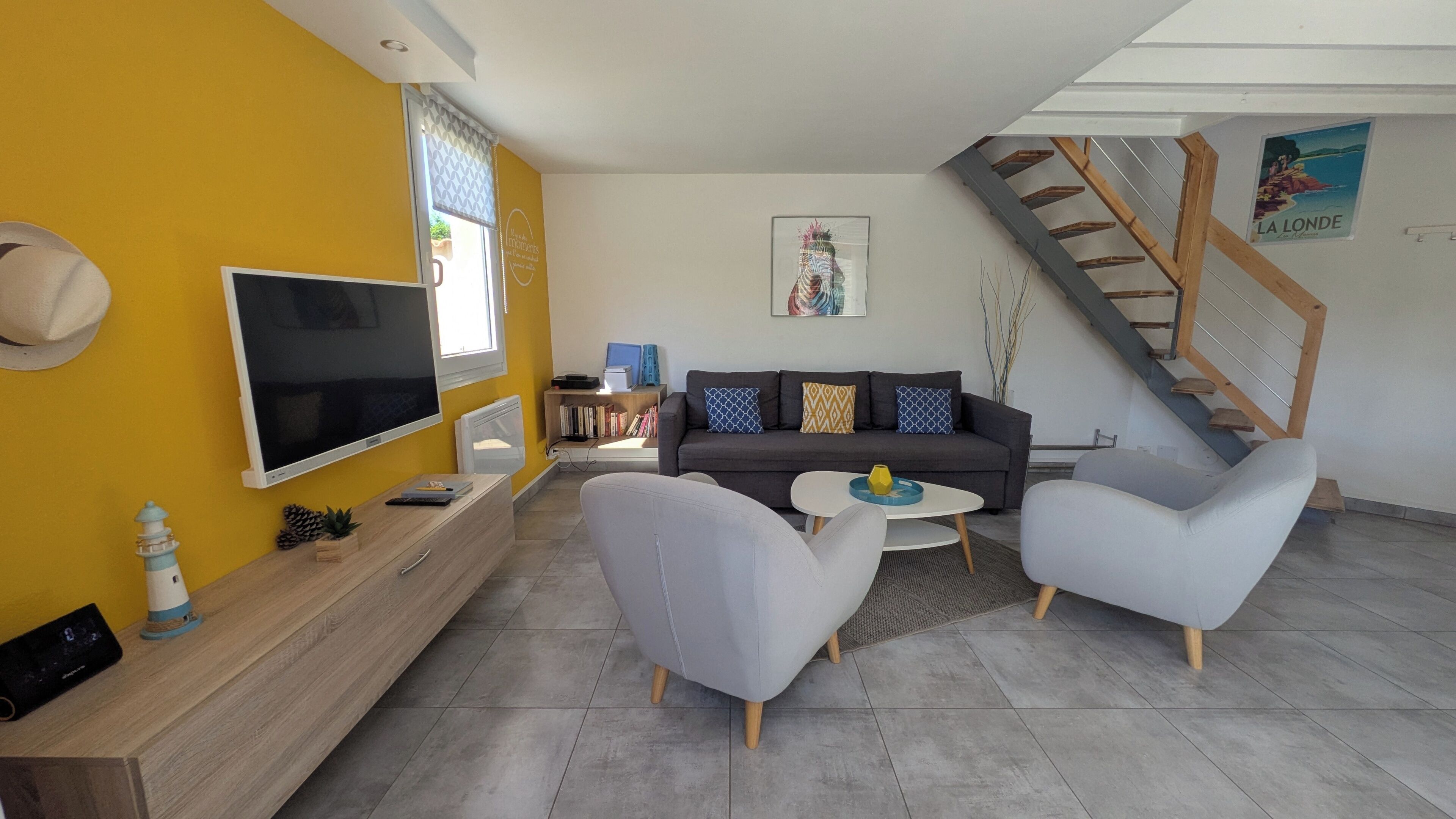 A modern living room with a sofa, two armchairs, a TV, and a bookshelf.
