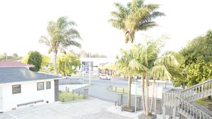 A hotel with a parking lot, palm trees, and a staircase leading to the entrance. - Pukekohe Motel (Pukekohe)
