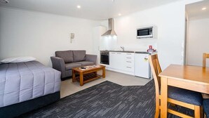 A compact hotel room with a bed, a sofa, a small kitchen area, and a dining table. - Pukekohe Motel (Pukekohe)