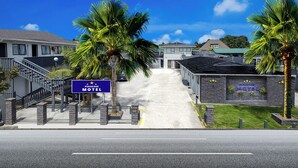 A motel with a signboard, palm trees, and a staircase leading to the entrance. - Pukekohe Motel (Pukekohe)