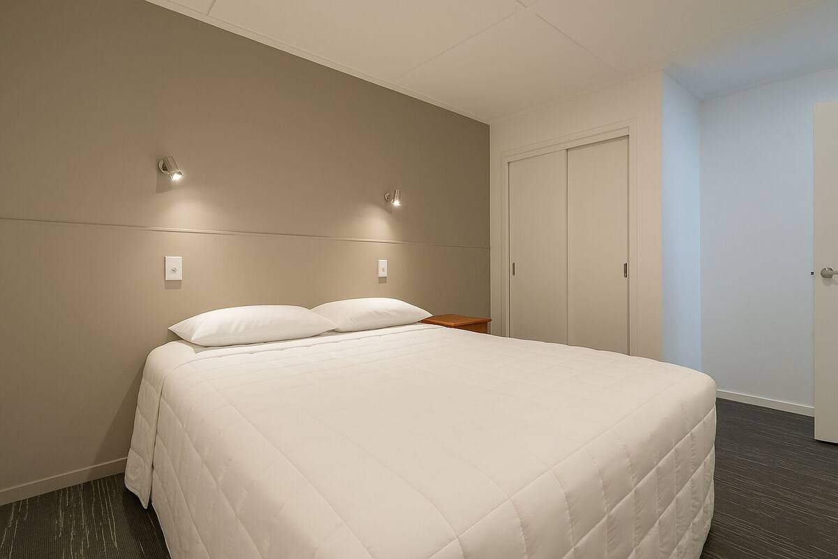 A hotel room with a large bed, two wall-mounted light fixtures, a wooden nightstand, and a closed door.