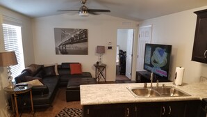 A living room with a sofa, a coffee table, a TV, and a kitchen area with a sink. - Newer Cavco Home in North Phoenix. Near Glendale, Arrowhead and Peoria (Glendale)