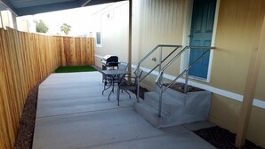 A patio with a concrete floor, a wooden fence, a barbecue grill, a table with chairs, and a blue door. - Newer Cavco Home in North Phoenix. Near Glendale, Arrowhead and Peoria (Glendale)