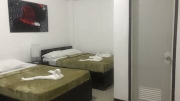 Habitación de hotel con dos camas, cada una con cubrecama verde y toallas blancas. Hay un cuadro en la pared y una puerta con un respiradero.