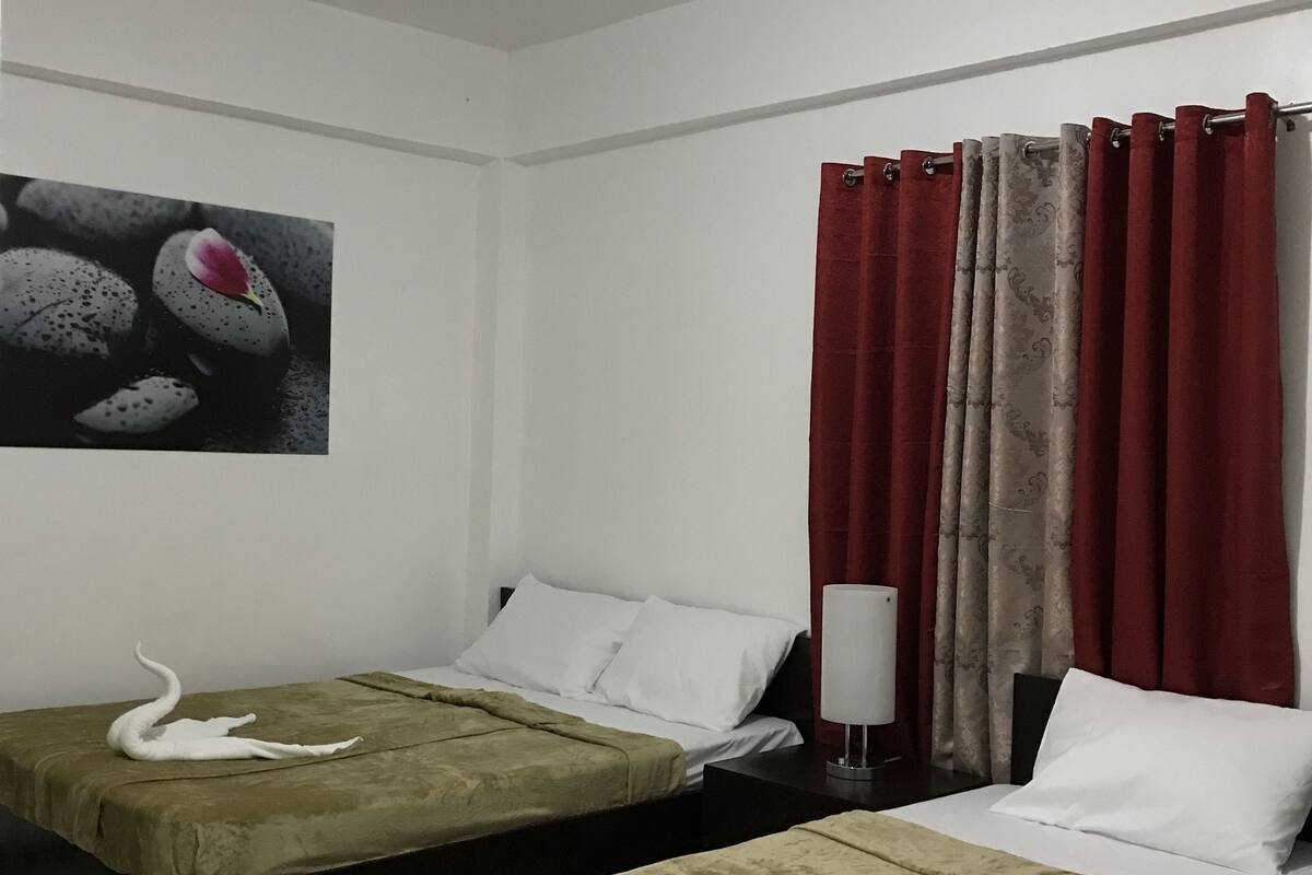 Ein Hotelzimmer mit zwei Betten, einem Bild an der Wand und einem Fenster mit roten Vorhängen.
