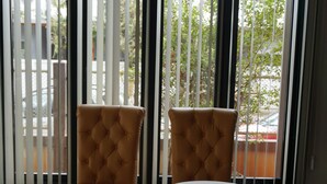 Habitación con dos sillones marrones con textura y una mesita blanca, unidad de aire acondicionado blanca en la parte superior, y vista a través de persianas verticales.