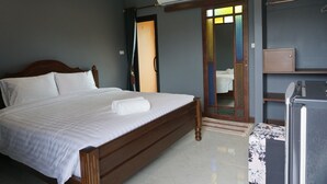 Un dormitorio con cama de madera, una mesita con mantel floreado, un armario y un espejo con marco decorativo.