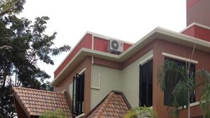 Un edificio de dos pisos con techo de tejas, un balcón y un pequeño jardín.