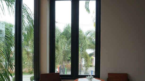 Una habitación con ventanas amplias, suelo de baldosas y dos sillas de madera alrededor de una pequeña mesa.