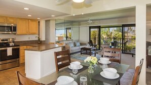 A modern kitchen with a central island, a dining area with a glass table, and a balcony with outdoor seating. - Amazing View ~ Amazing Price ~ Amazing Location  (Princeville)