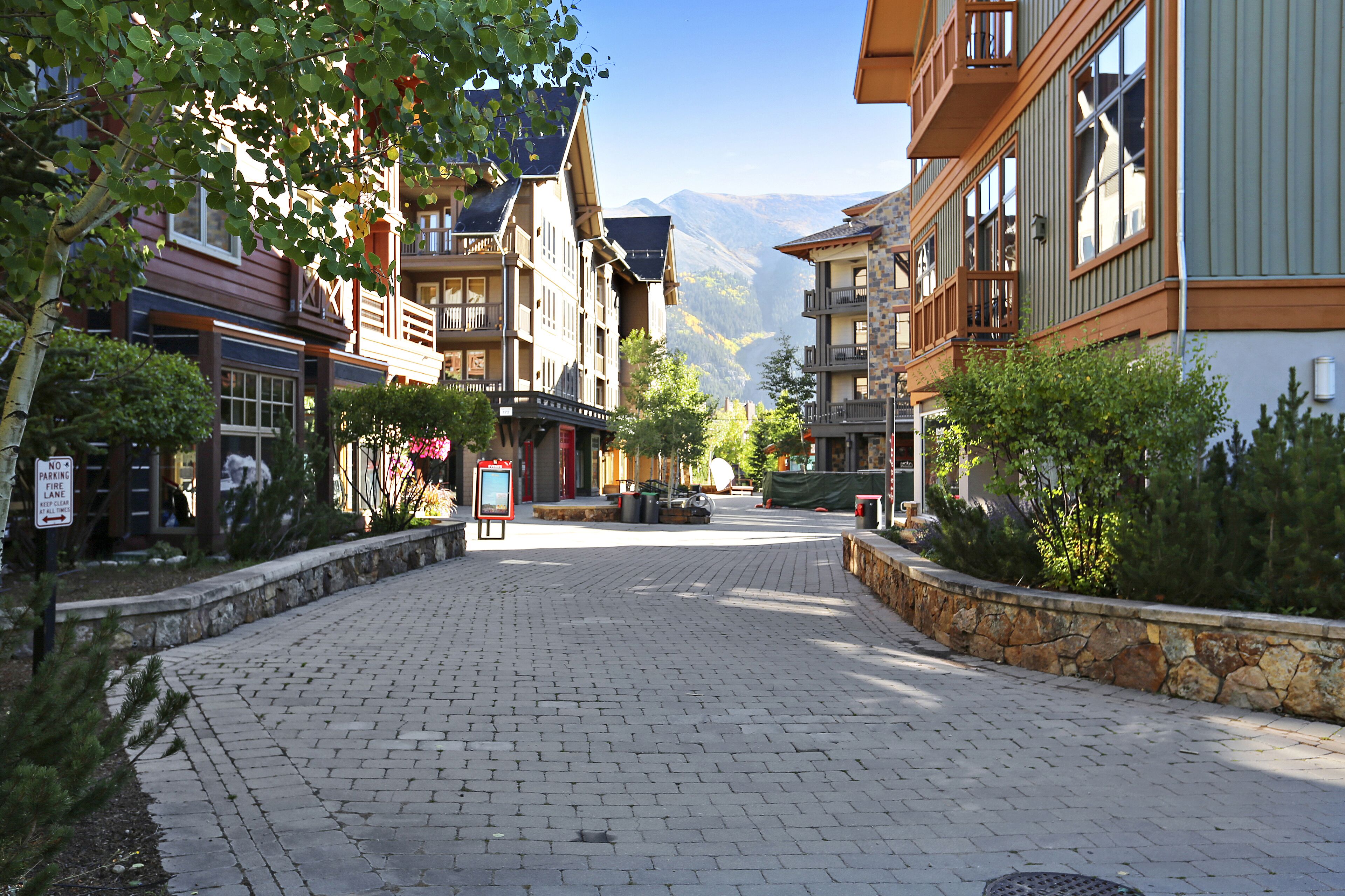 A paved street lined with multi-story buildings, some with balconies, in a mountainous area.