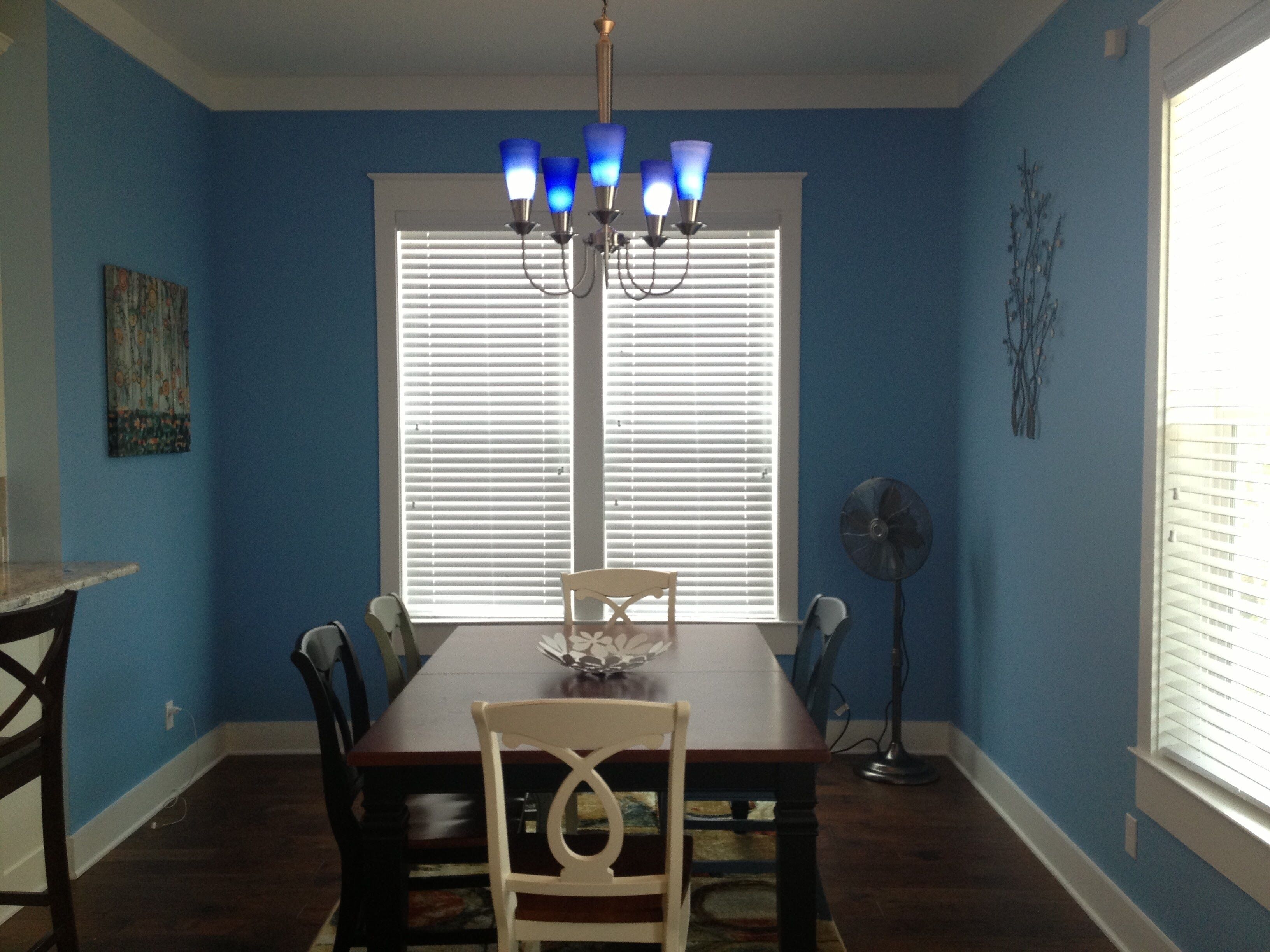 A dining room with a wooden table, chairs, a chandelier, and a window with blinds.
