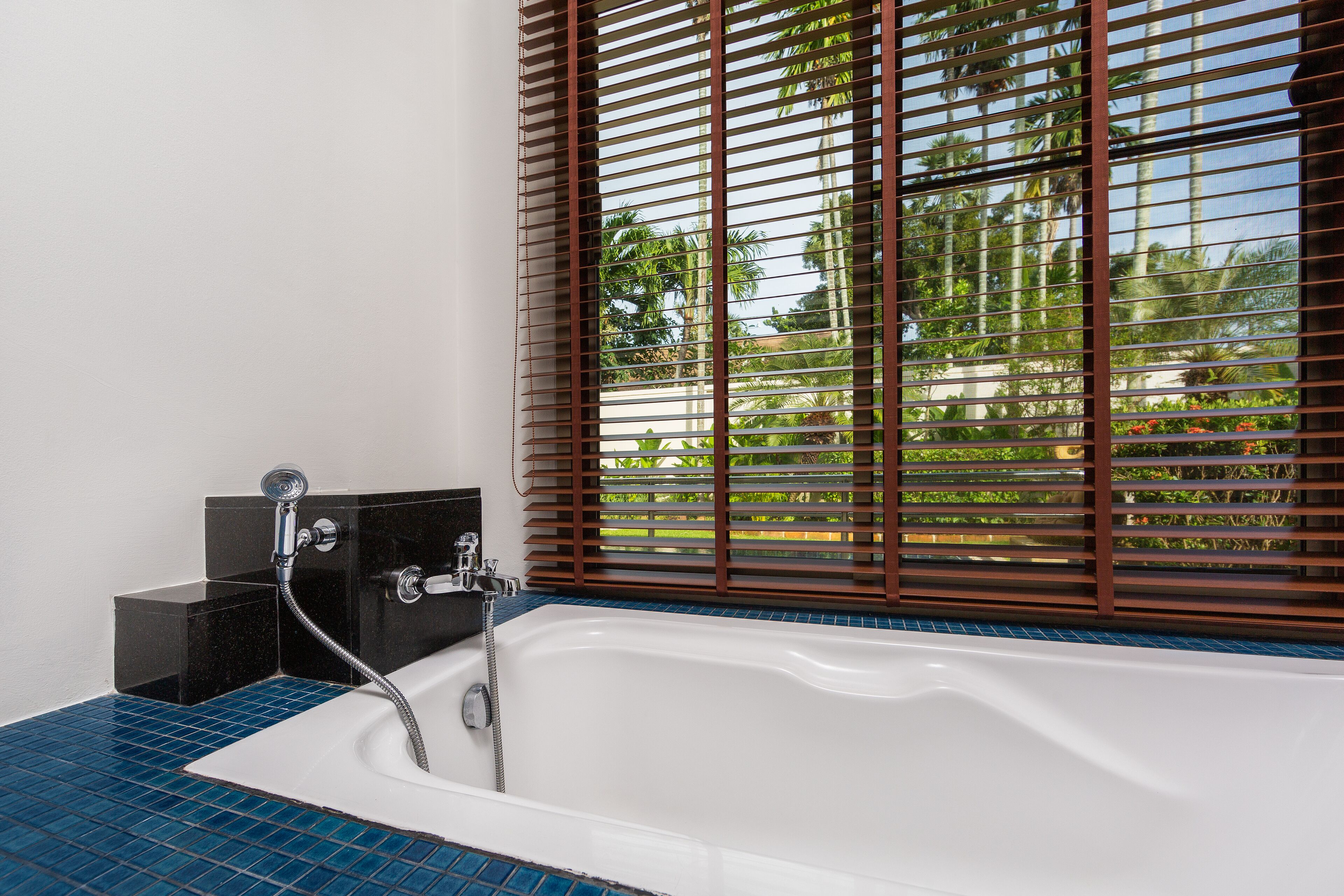 Ein Badezimmer mit Badewanne, Dusche und einem Fenster mit Jalousien.