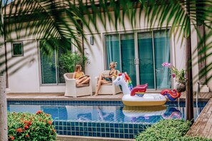 A pool area with two lounge chairs, a unicorn float, and potted plants. - Niche Villas by TropicLook (Rawai)