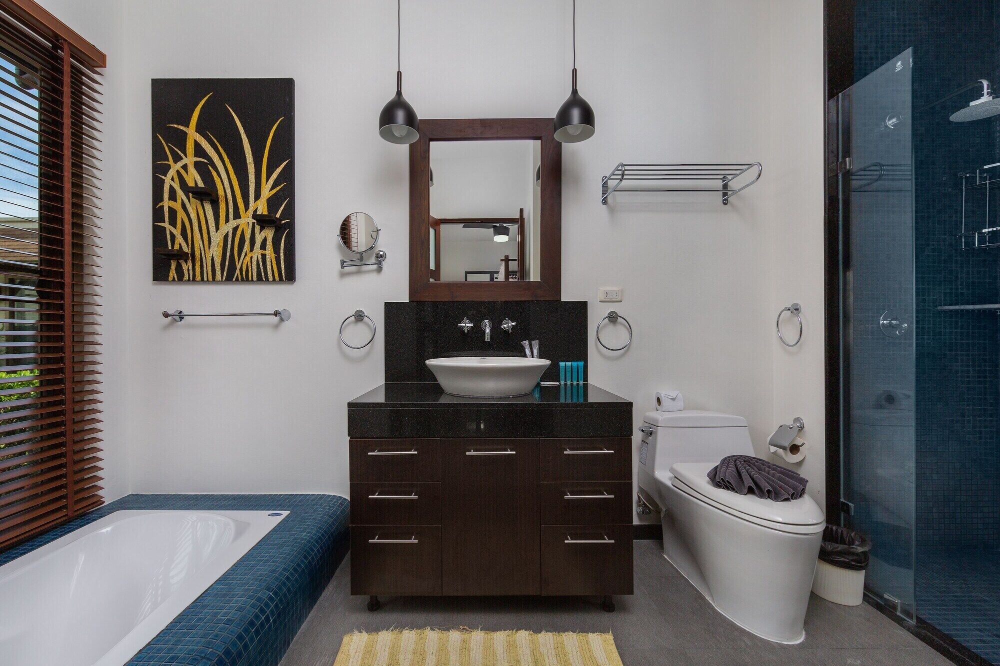 A modern bathroom with a large sink, dark wooden vanity, a mirror above the sink, a towel rack, a toilet, and a shower area.