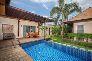A swimming pool with a wooden deck, a covered patio, and a dining area with outdoor furniture. - Niche Villas by TropicLook (Rawai)