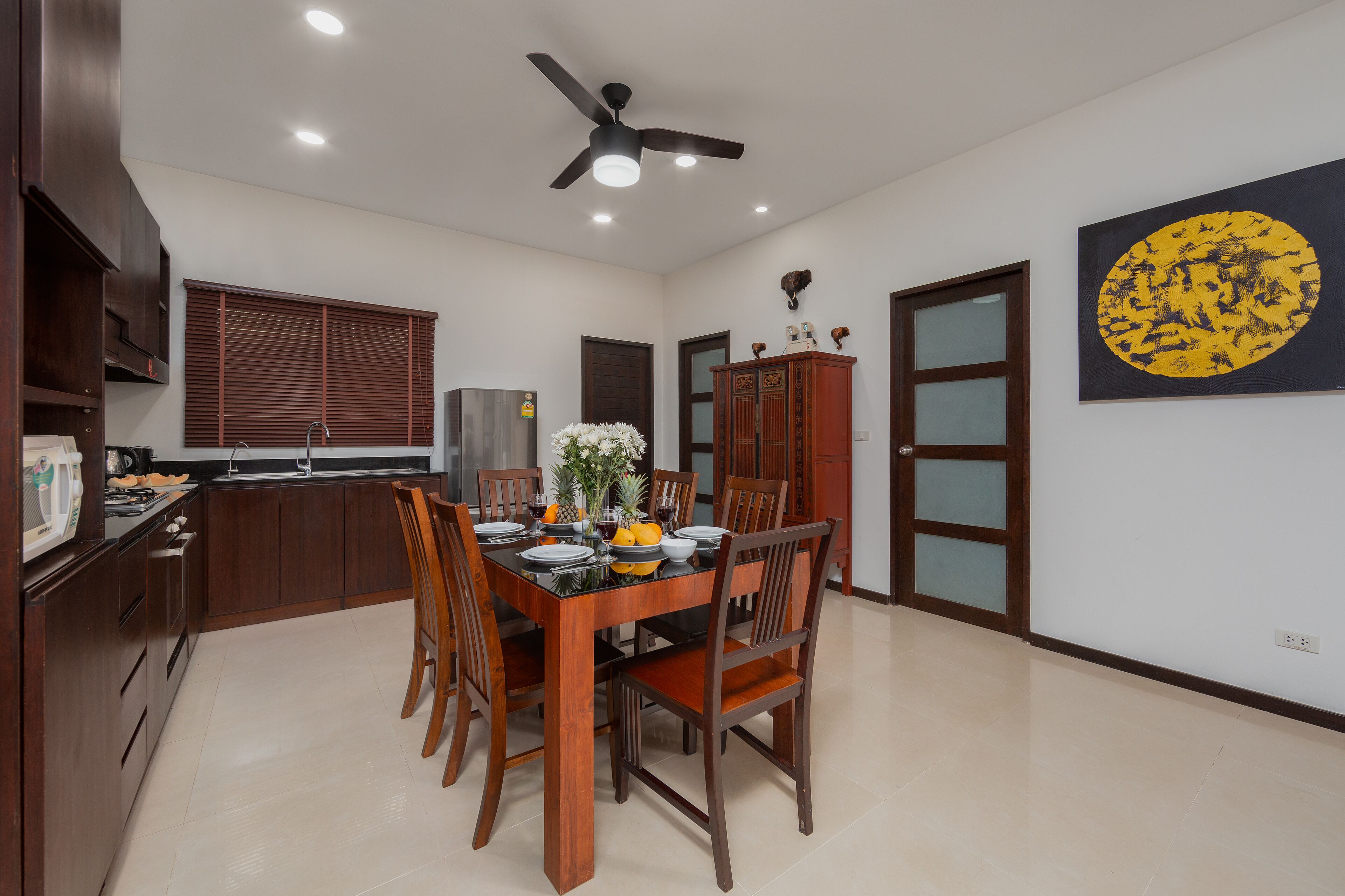 A dining area with a wooden table set for four, surrounded by chairs. A ceiling fan is visible above the table.
