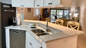 A kitchen with white cabinets, a dishwasher, a sink, and a dining area with chairs.