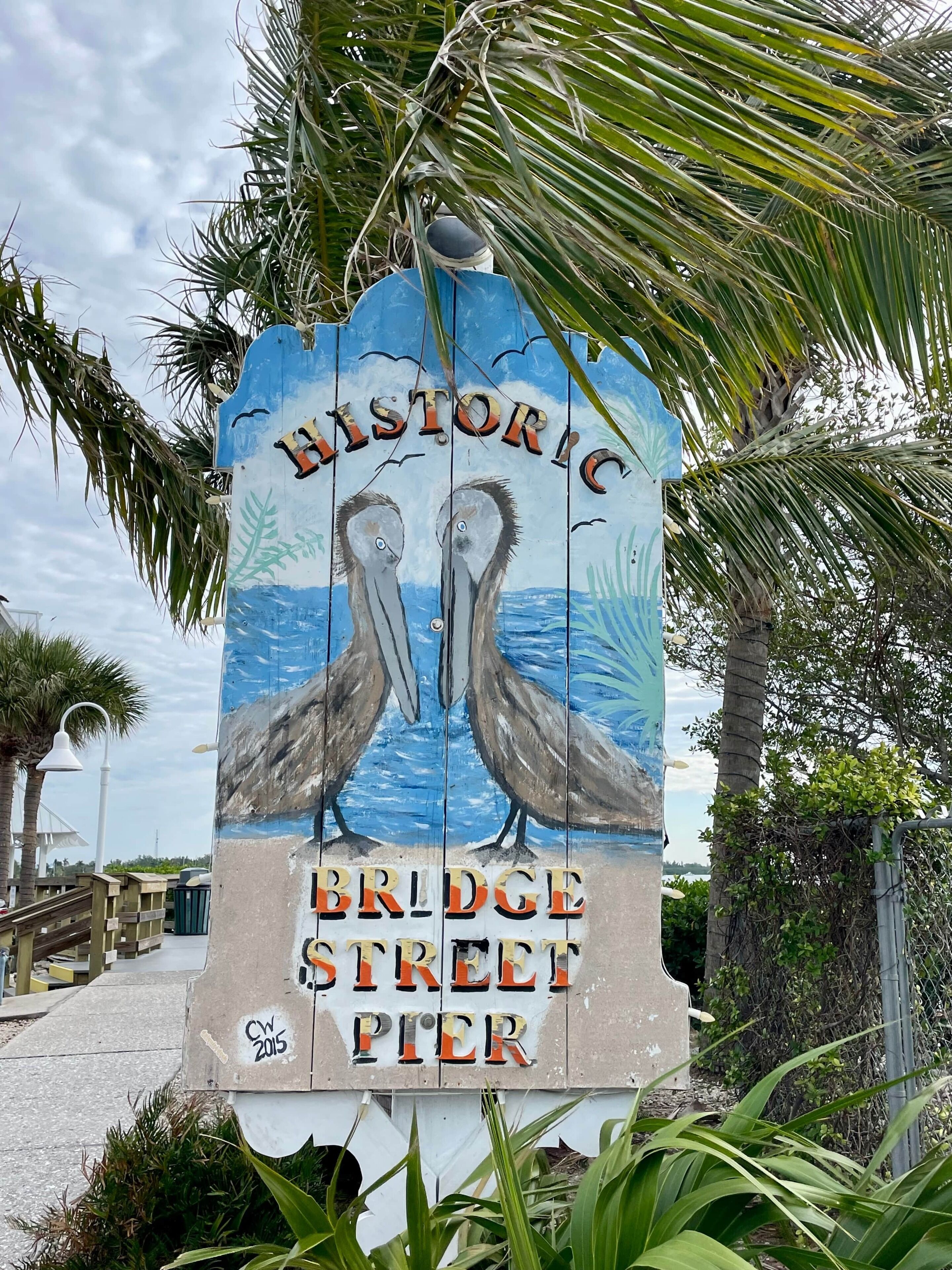 Een historiek straatnaambord met twee pelikanen en de tekst 'BRIDGE STREET PIER'.