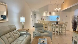 A modern living room with a sofa, a coffee table, and a dining area with chairs and a chandelier.