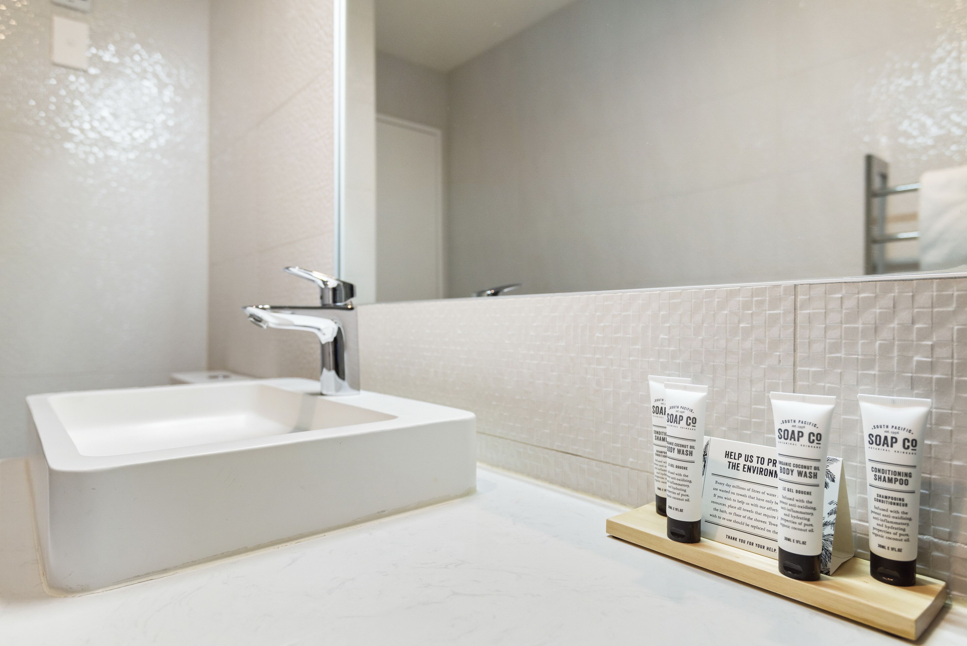 A bathroom with a white sink, a mirror, and three soap dispensers on a wooden shelf.