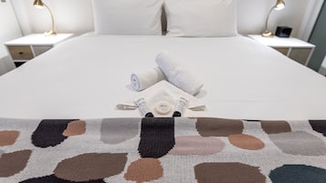 A neatly made bed with white linens, two bedside lamps, and a patterned throw blanket.