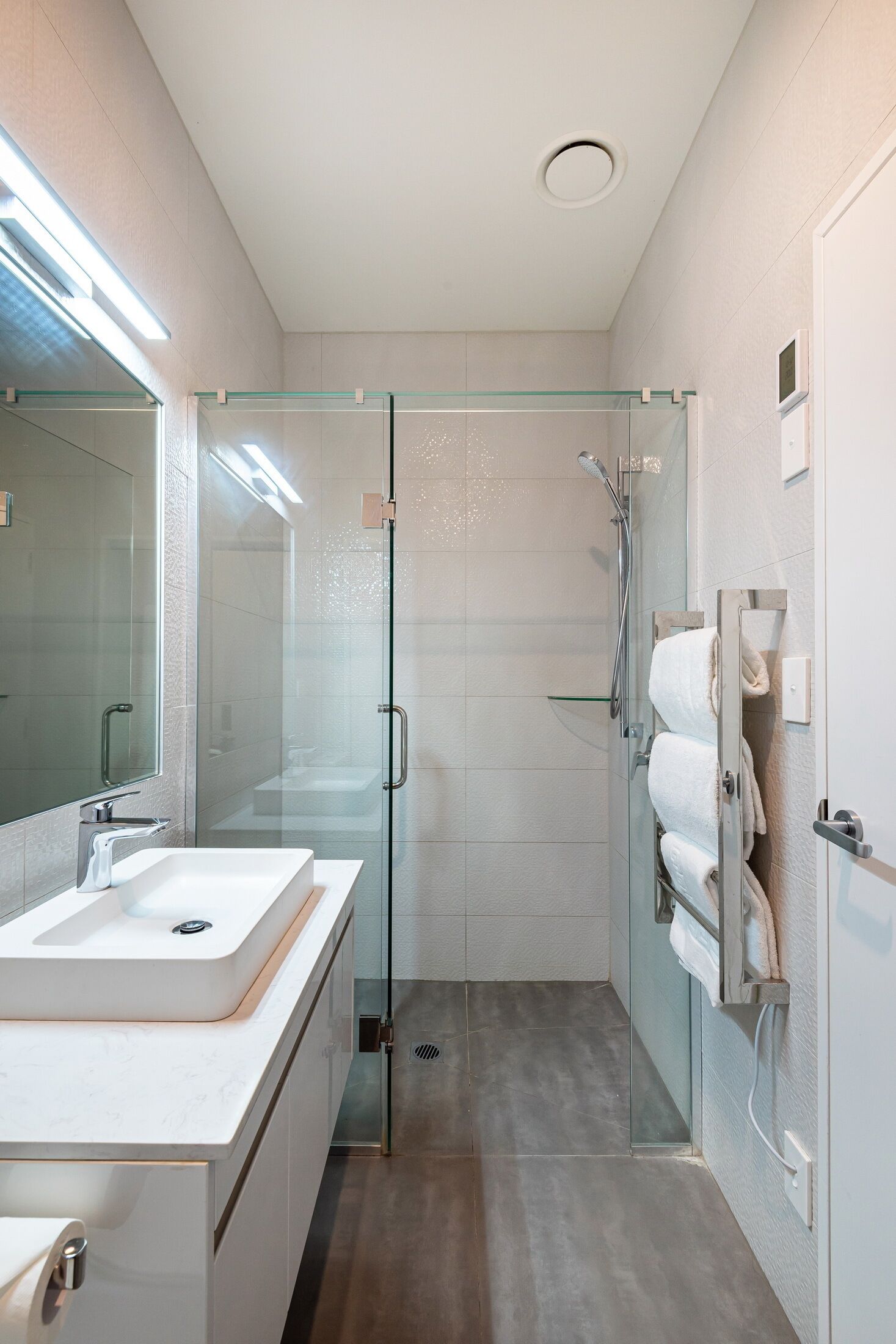 A modern bathroom with a glass-enclosed shower, a white sink, and a mirror.