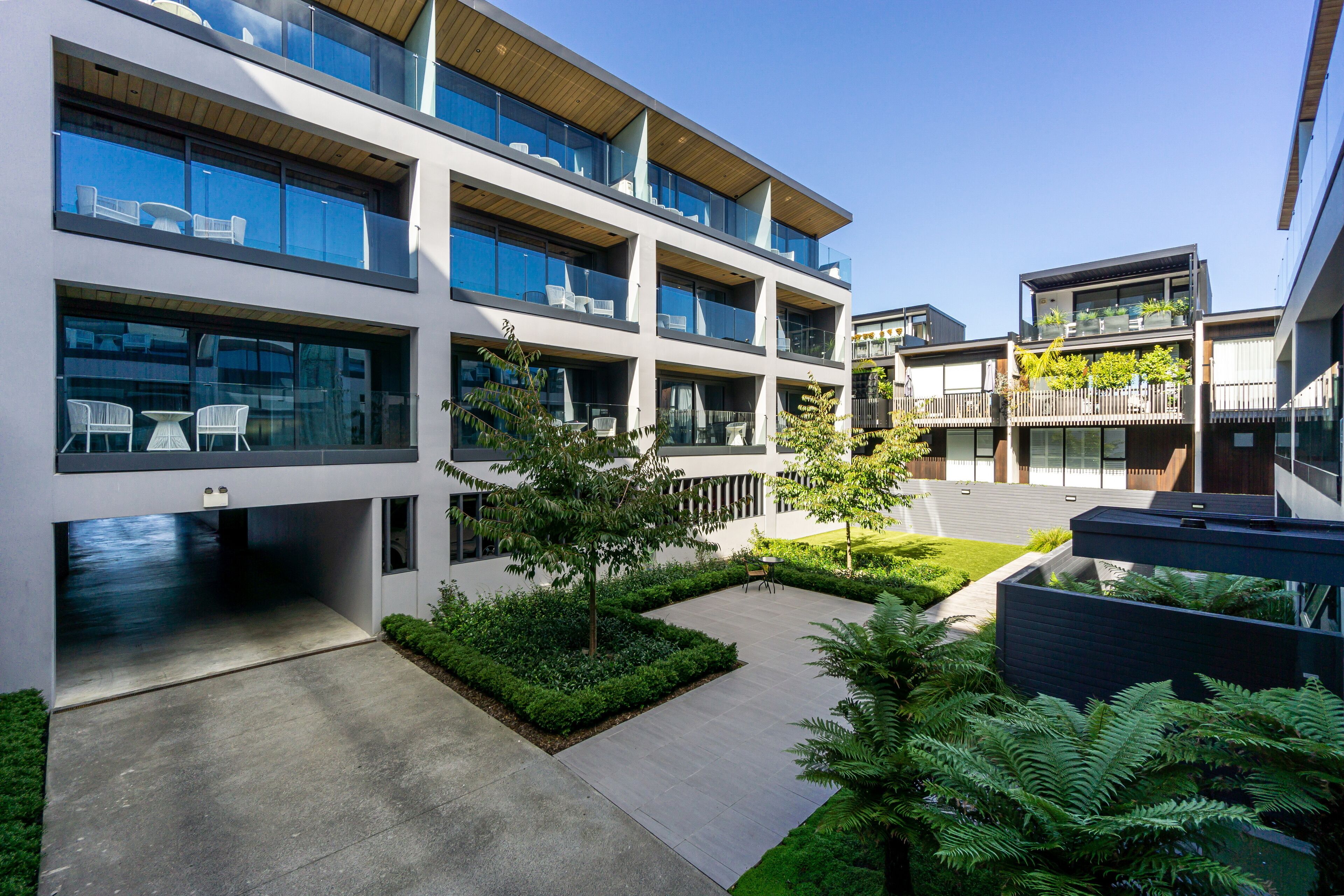 A modern multi-story building with balconies, outdoor seating, and a landscaped courtyard.