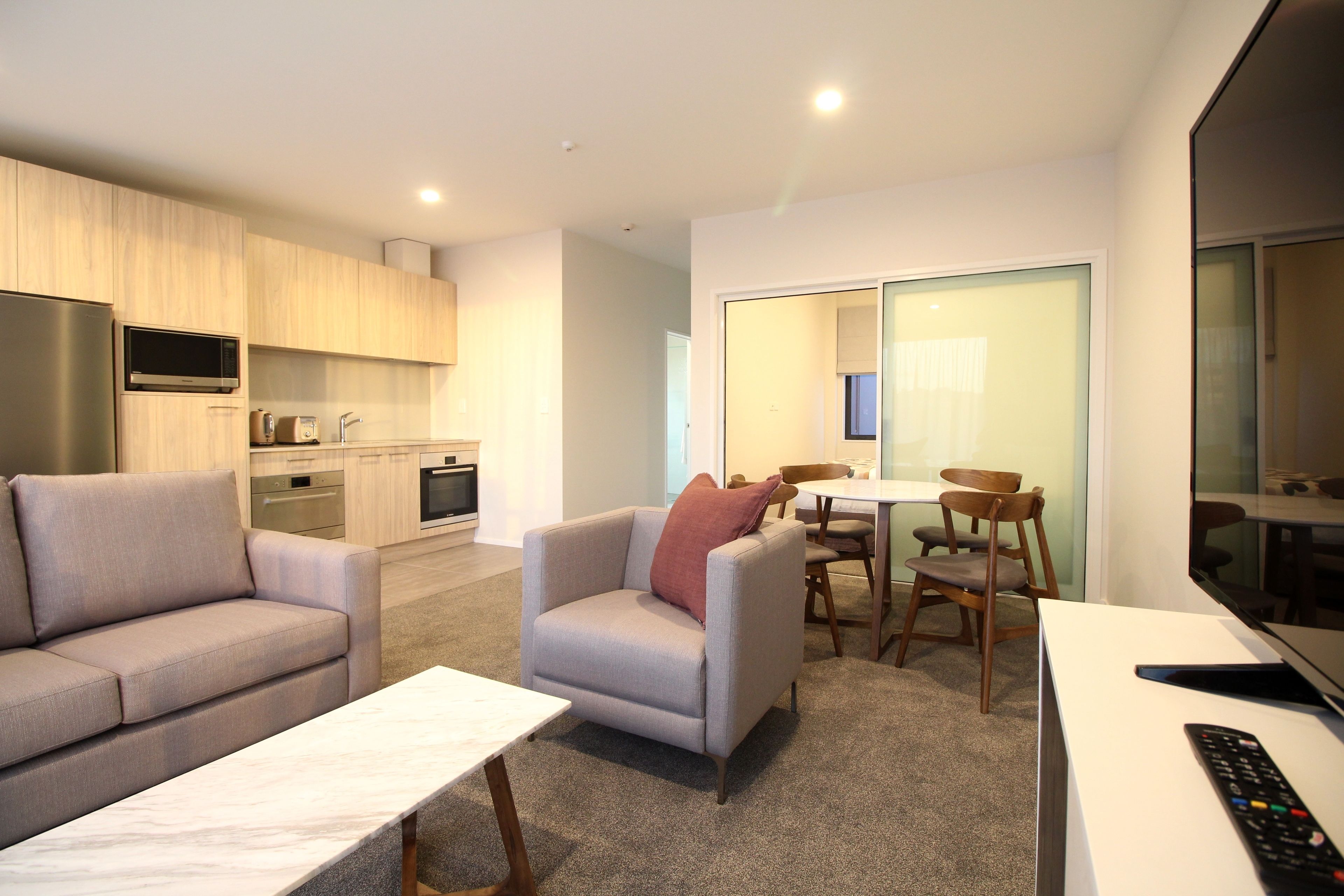 A modern living room with a sofa, armchair, and a coffee table. There is a TV and a remote control on a stand.