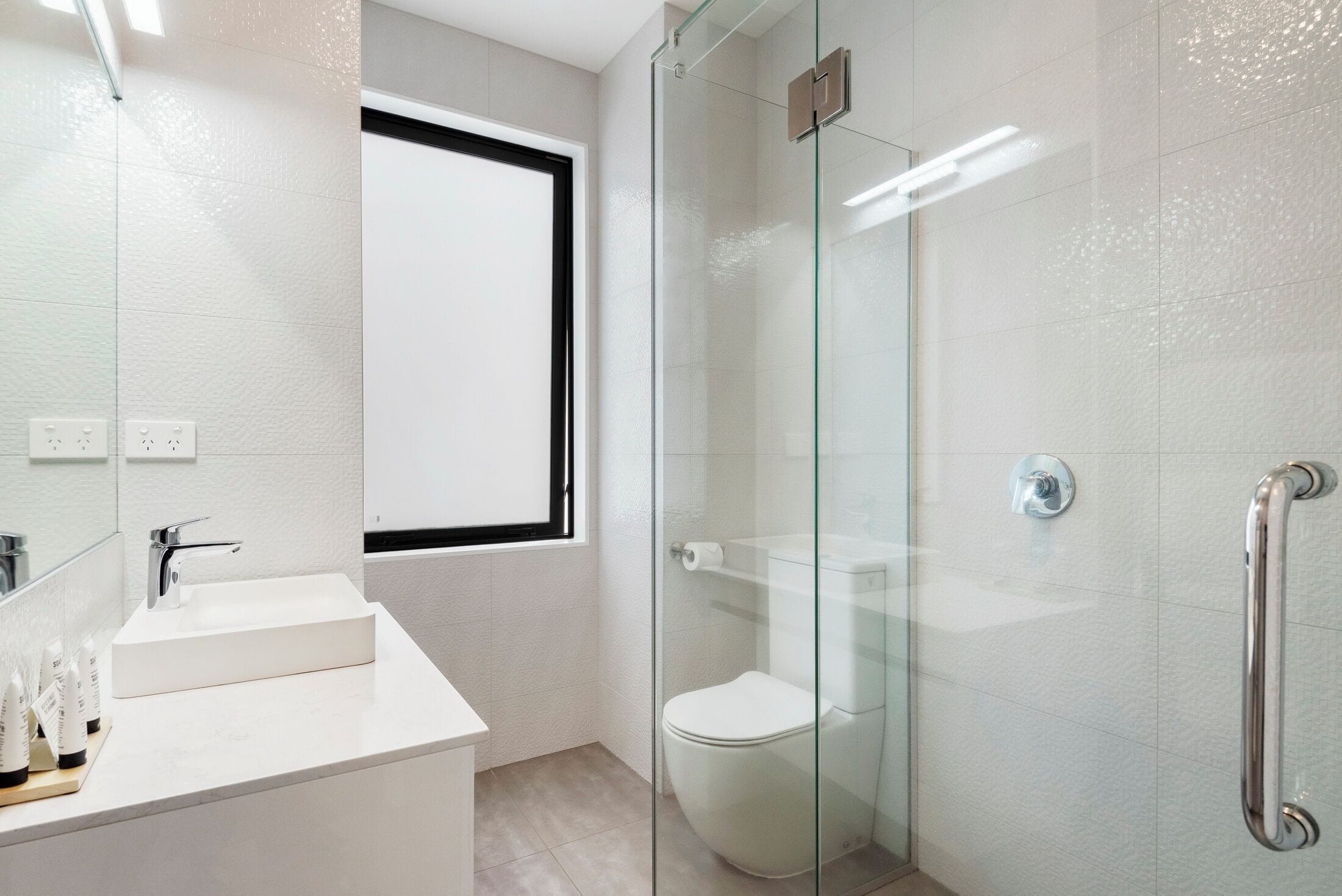 Un baño moderno con cabina de ducha de vidrio, lavabo blanco y retrete.
